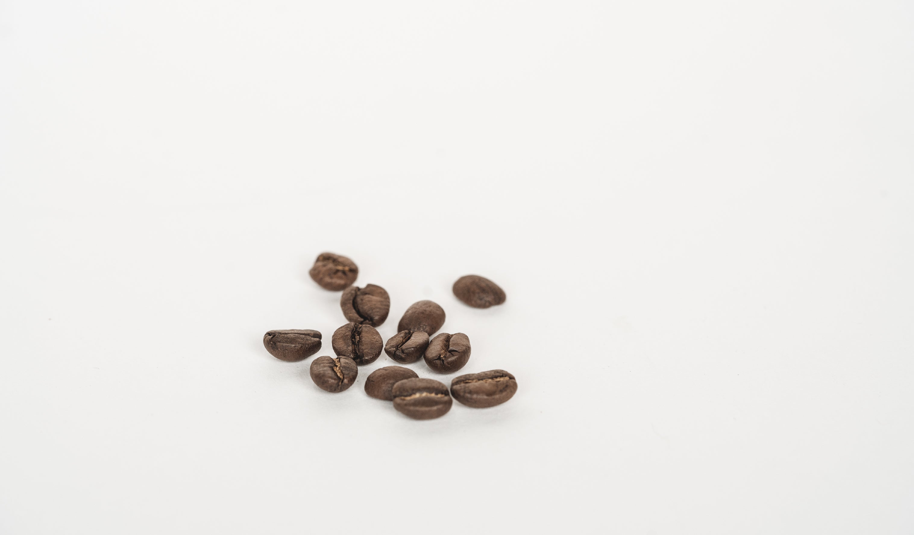 A handful of roasted coffee beans scattered on a white table.