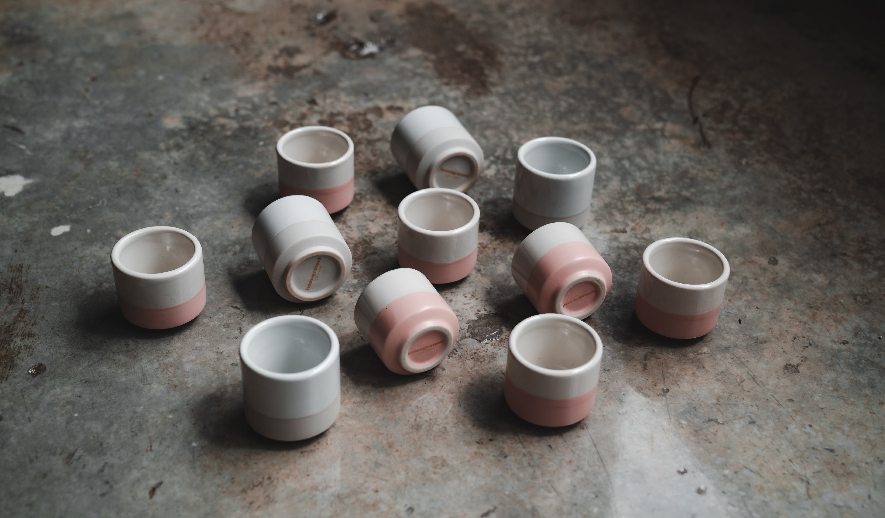 Ceramic cups with a simple, rustic design are placed on a textured surface. The lighting casts soft shadows, highlighting the cups smooth textures against a dark background.